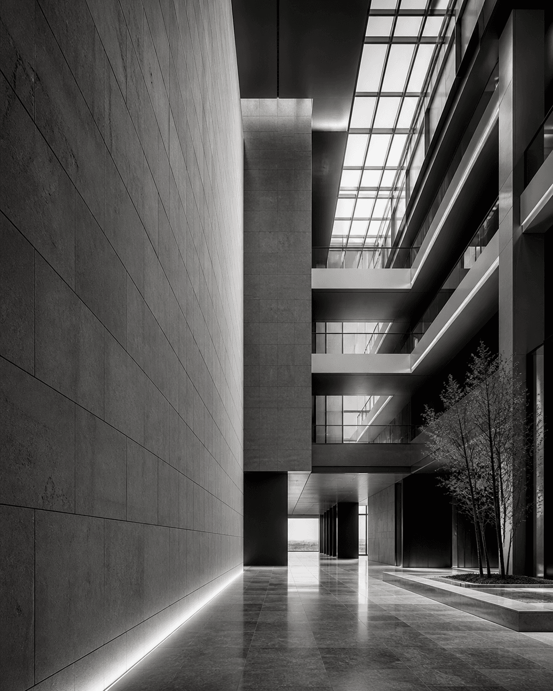 Tall atrium interior with stone surfaces, glass walls, and restrained lighting.